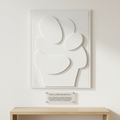 Framed abstract relief sculpture on a white wall with a wooden shelf below.